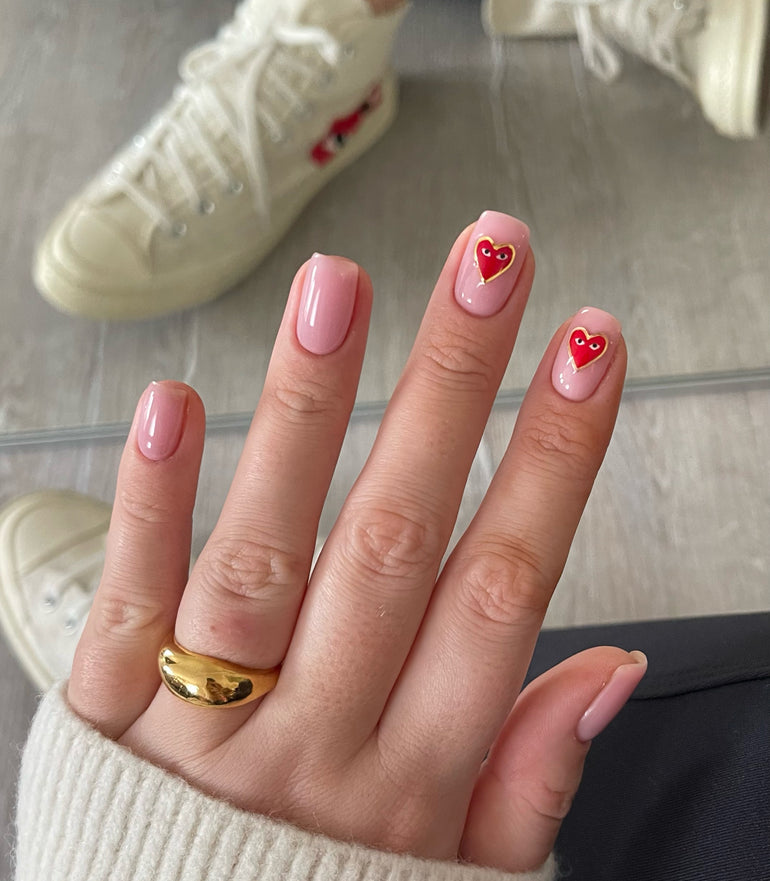 Pink gel nails with gold-lined red hearts with eyes