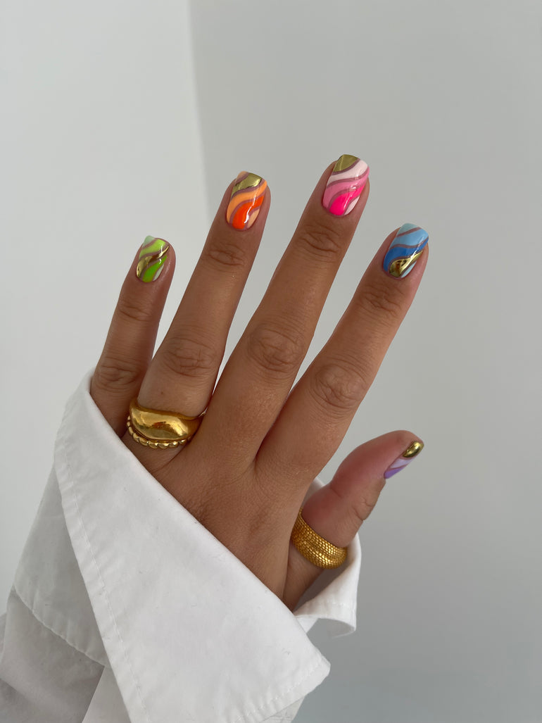 Multilcolour painted nails with gold jewellery and white shirt sleeve