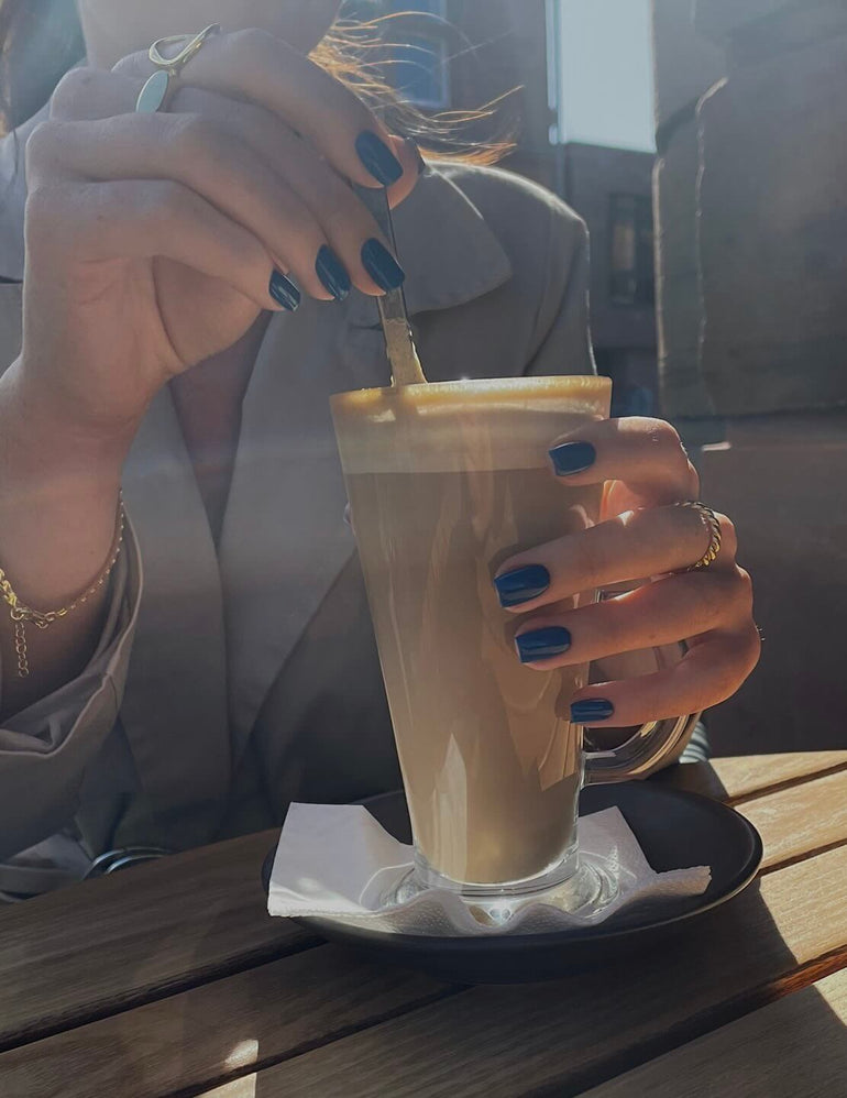 Deep blue gel nails holding a glass of coffee