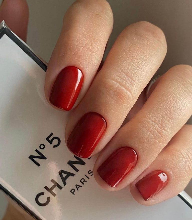 Mid red gel nails holding Chanel No. 5 packaging