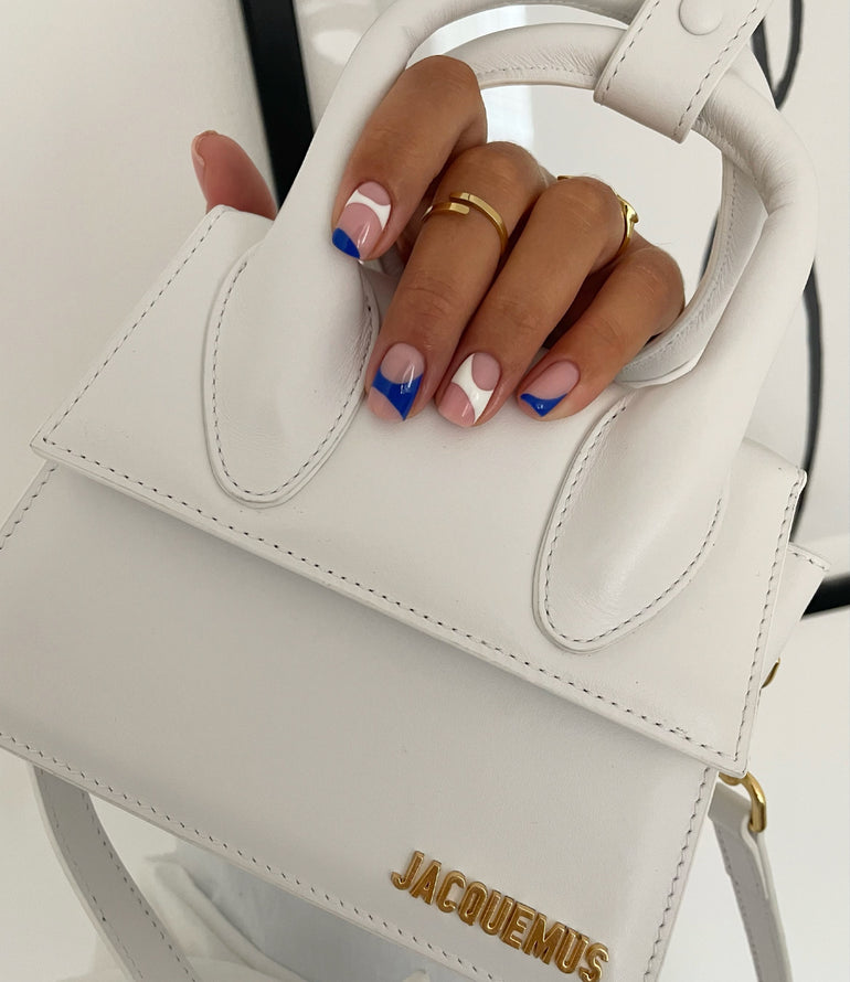 White and navy blue gel nails holding white Jacquemus handbag