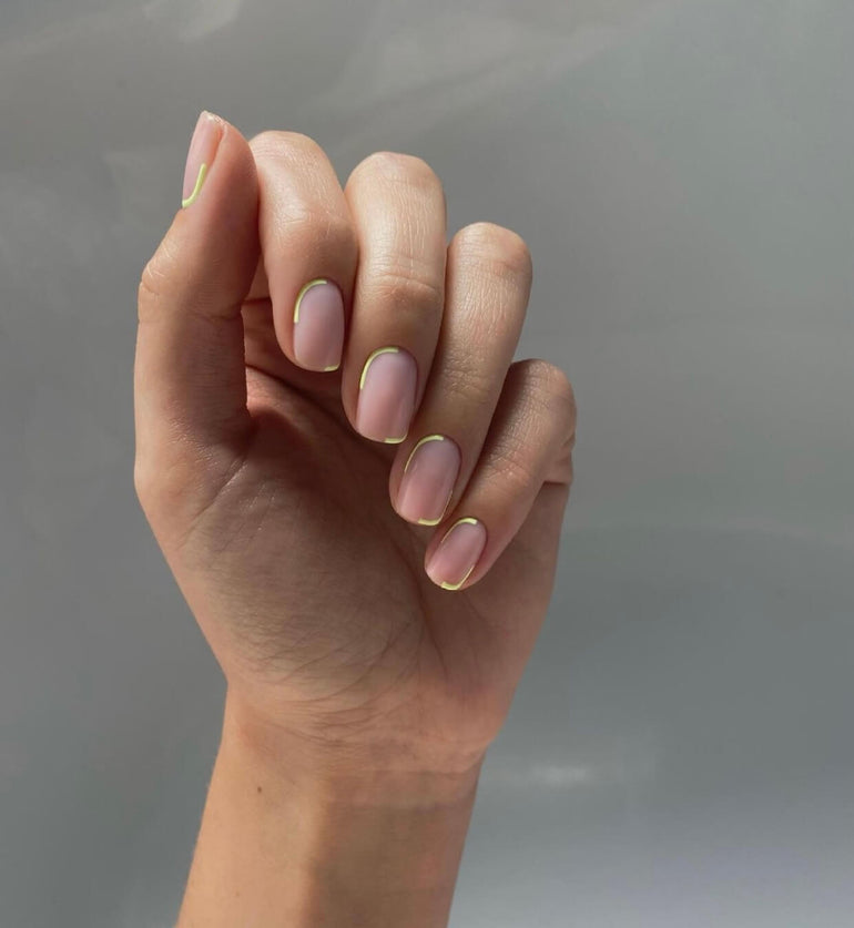 Nude pink gel nails with off-center gold tips and cuticles