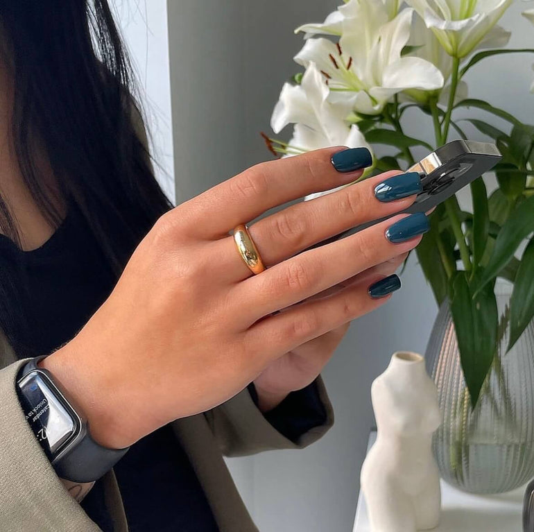 Deep turquoise gel nails holding an iphone over a background of white flowers